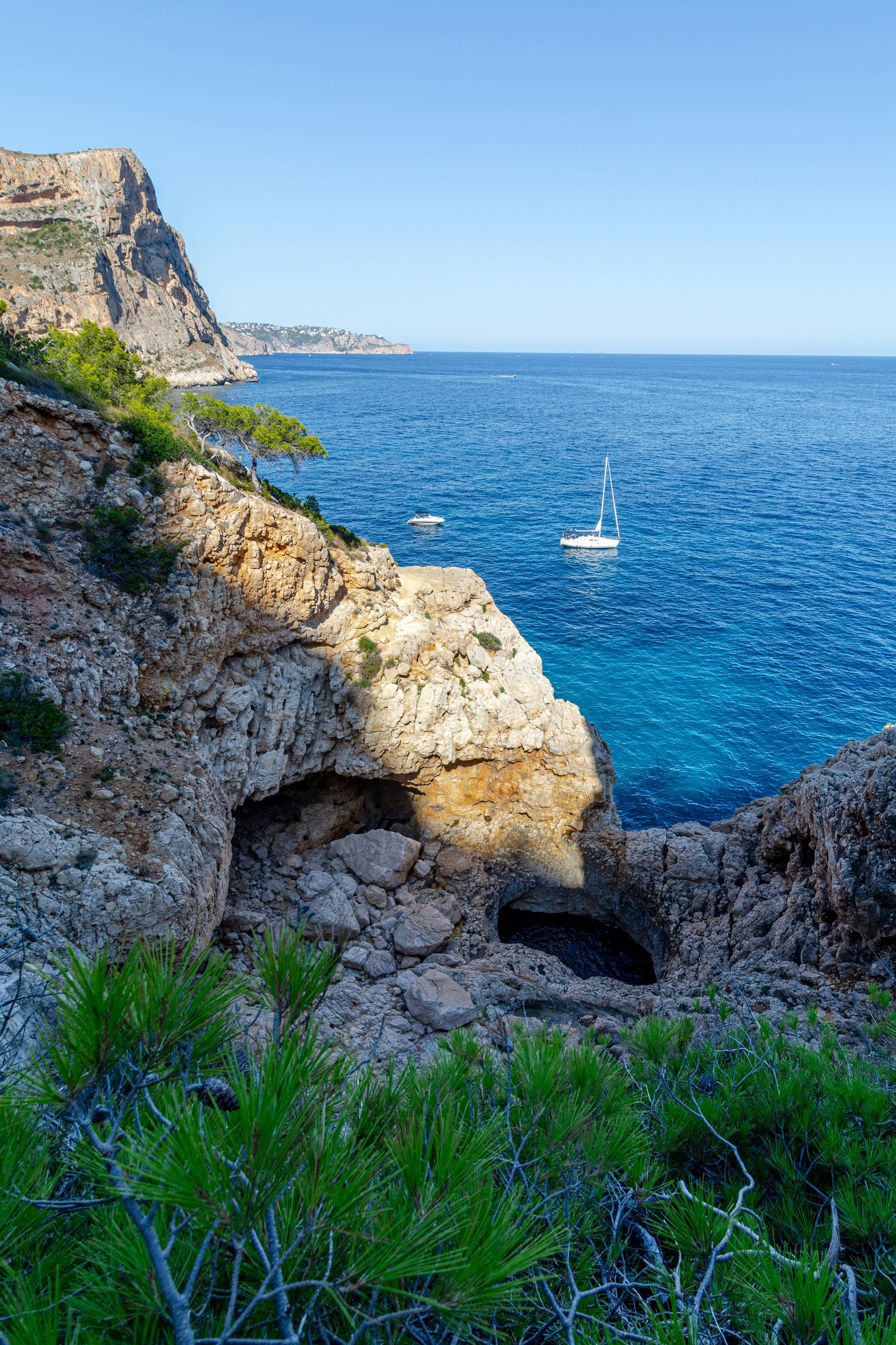 Piccola barca a vela bianca al largo della costa rocciosa di Cala Moraig